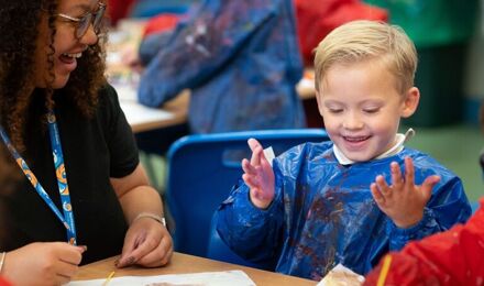 Boy wearing and apron, holding hands up covered in paint